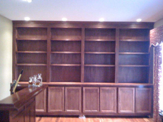 Floor-to-ceiling walnut built-in bookcase with open shelving and cabinet base